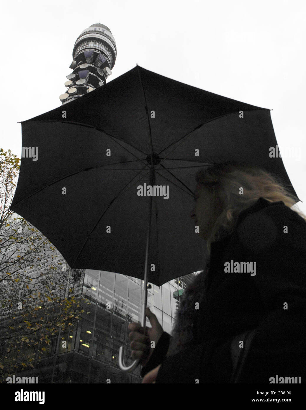 Eine Frau mit einem Regenschirm geht am Telecom Tower im Zentrum Londons vorbei. Stockfoto