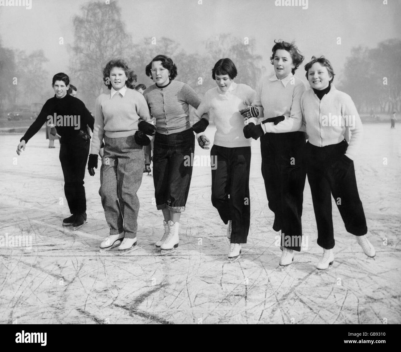 Mädchen Arm in Arm auf Wimbledon Common, so dass das Beste aus dem kalten Wetter einige freie Skating auf dem gefrorenen Teich genießen. Stockfoto