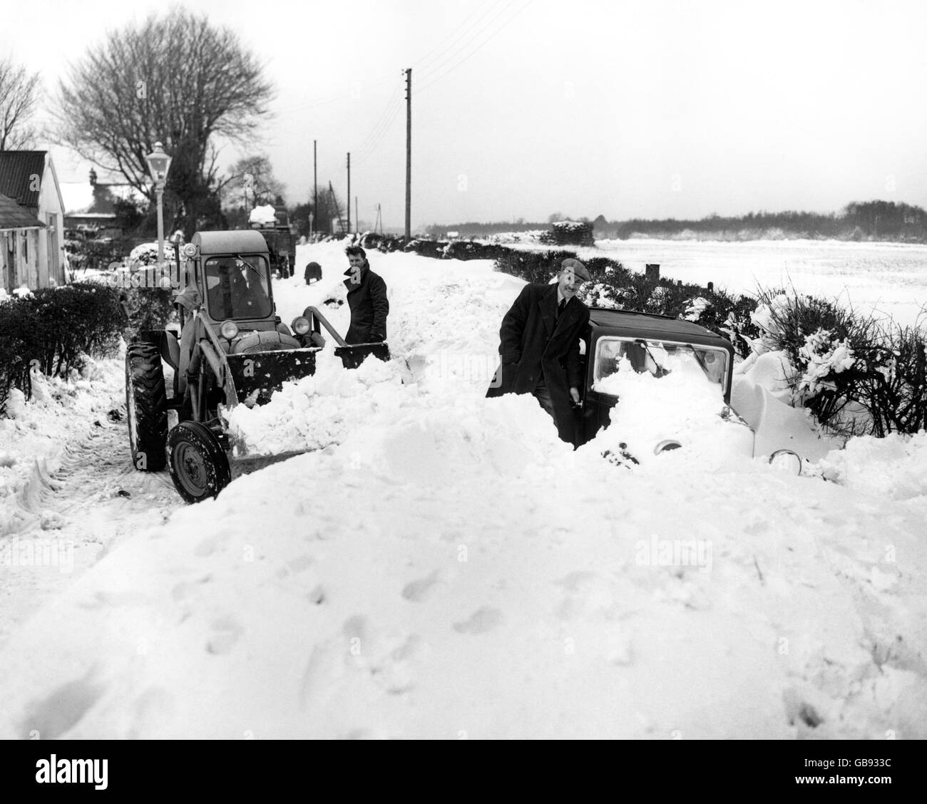 Ein Bulldozer macht einem Auto den Weg frei, das im Schnee auf der Biggin Hill nach Westerham Road in Kent gehalten wird. Stockfoto