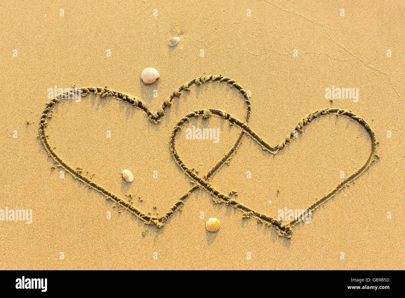 Zwei Herzen auf einem sandigen Strand gezogen. Stockfoto