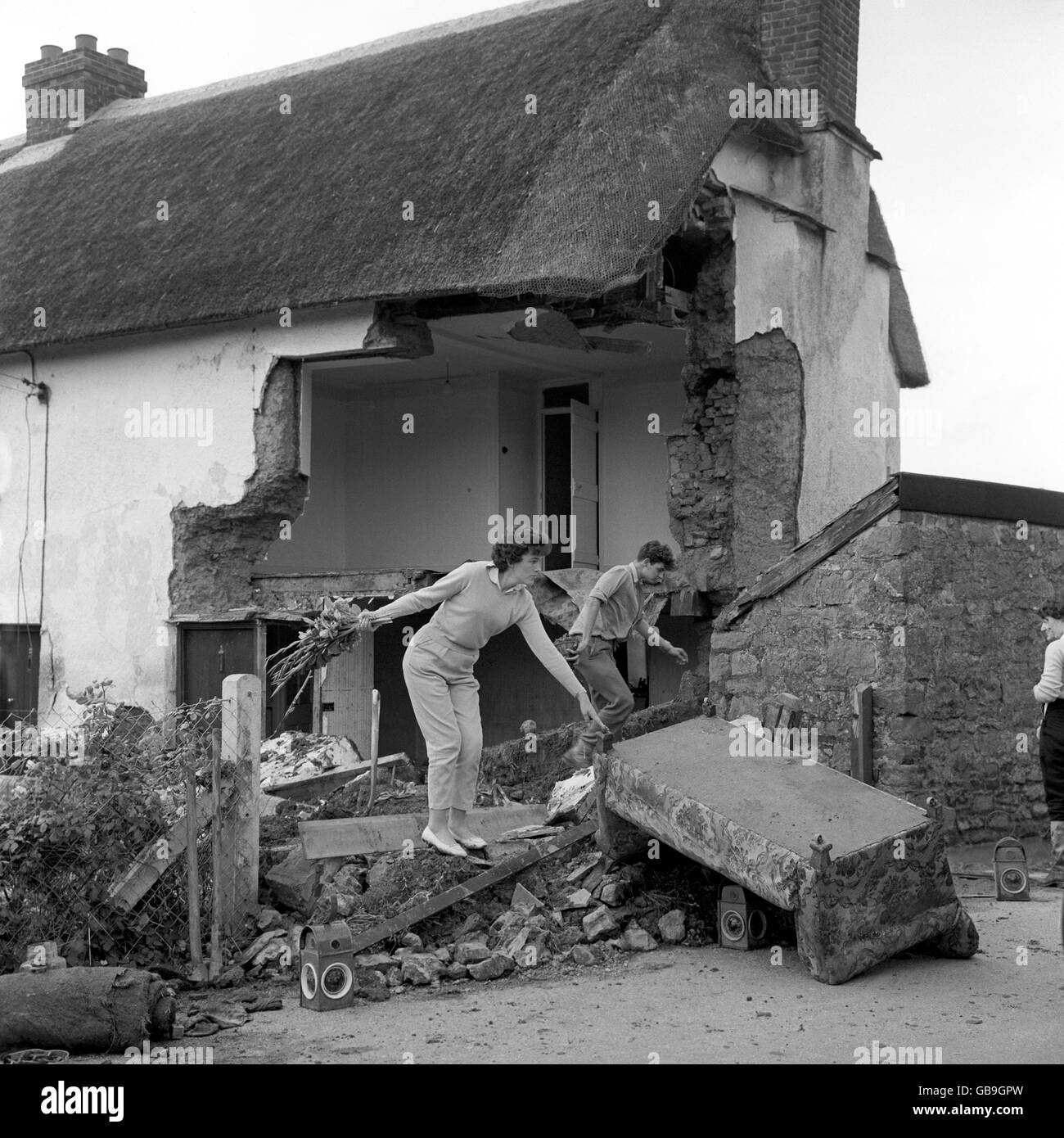 Unter einem intakten, gepflegten Strohdach sucht ein Paar nach Habseligkeiten in den mit Wasser bedeckten Trümmern, die die Ecke des Devonshire Cottage in Exton bildeten, die durch ausgedehnte Überschwemmungen nach andauerndem sintflutartigen Regen verursacht wurden. Stockfoto