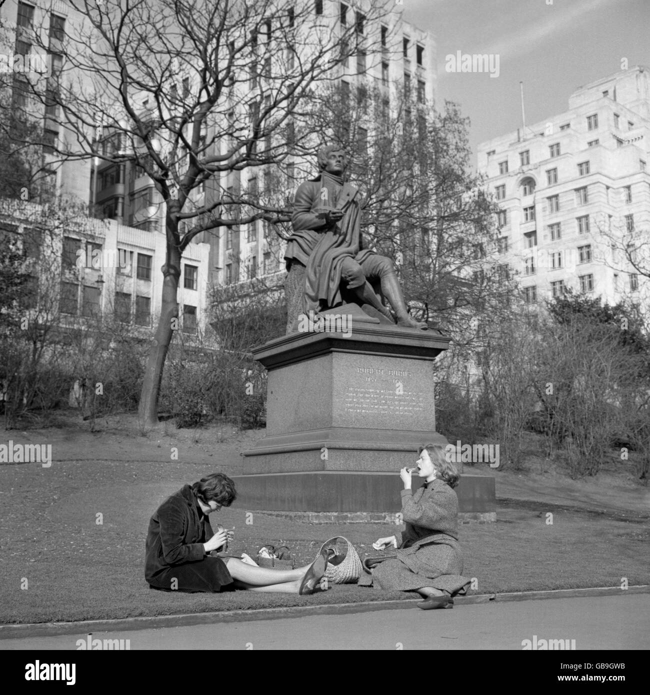 Erinnerungen an den großen Frost schmelzen in der milderen Frühlingsluft, während diese Mädchen ein Picknick zum Mittagessen bei der Statue von Robert Burns in den Gärten am Victoria Embankment, London, genießen. Stockfoto