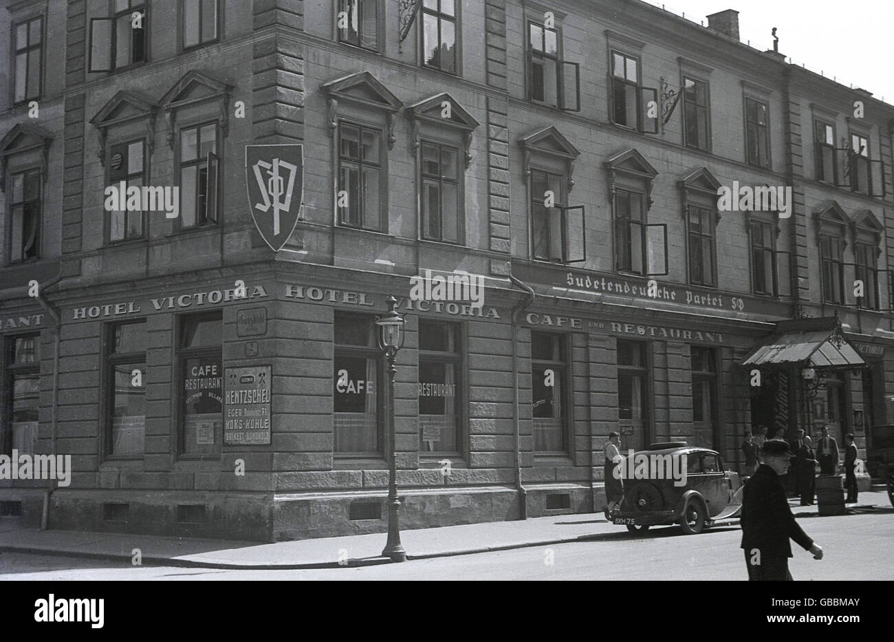 der 1930er Jahre zeigt historische Bild das Hauptquartier der Sudeten Deutsch-Partei (SdP) über das Hotel Victoria in Cheb (Eger) in den Sudeten, in der Tschechoslowakei der Zwischenkriegszeit. Ein Auto mit einem britischen Nummernschild ist direkt außerhalb geparkt. Stockfoto