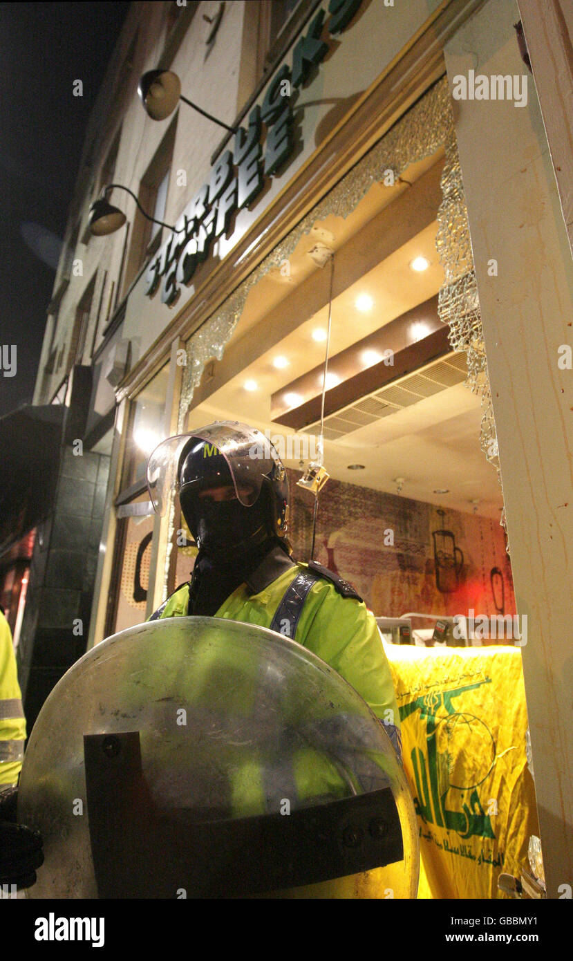 Vor einem beschädigten Starbucks steht ein Polizeibeamter in Bereitschaftskleidung, in der Nähe der israelischen Botschaft in London, wo Demonstranten gegen den Konflikt in Gaza protestieren. Stockfoto