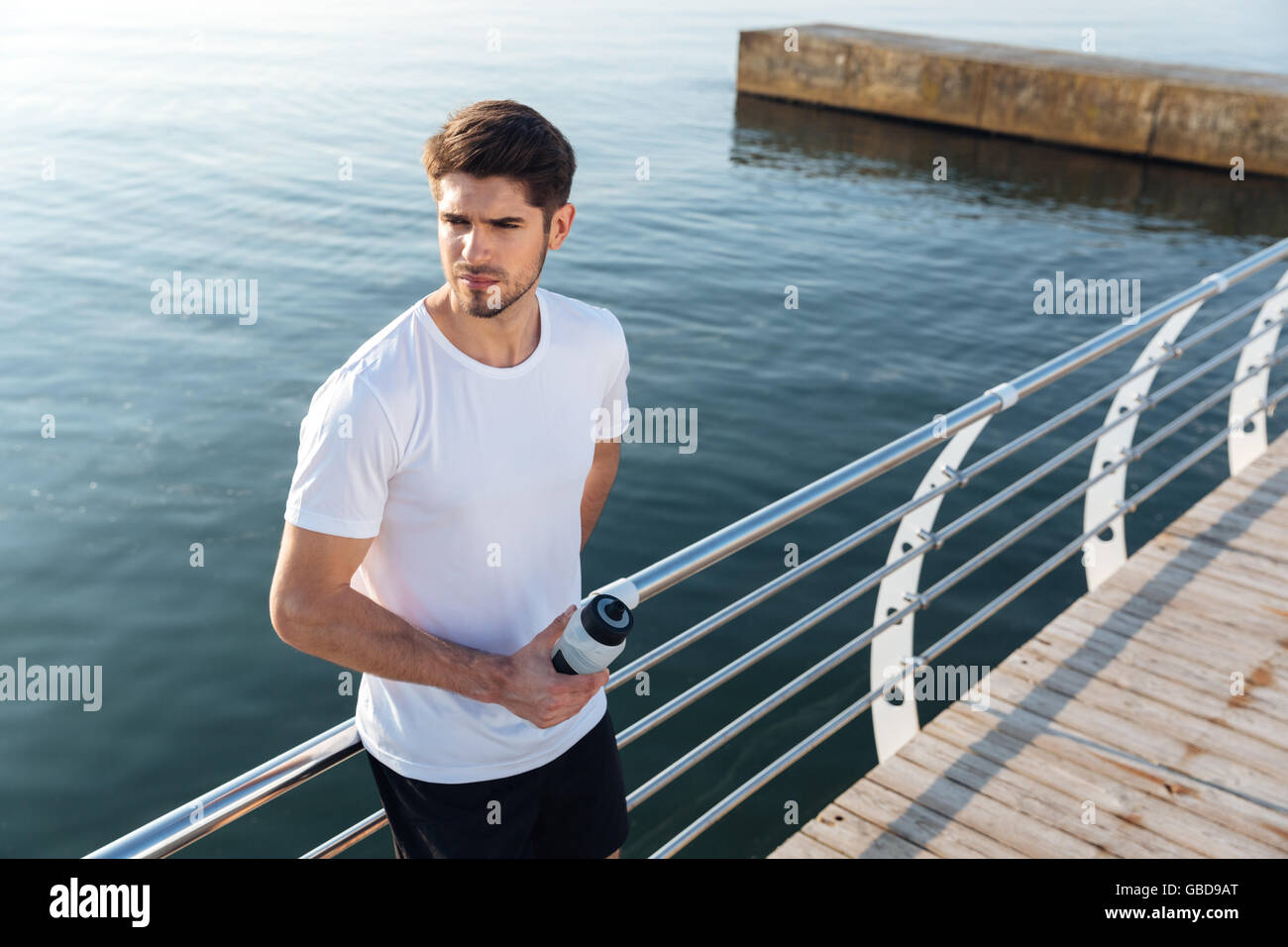 Hübscher Junge Sportler Stand in der Nähe des Meeres und Trinkwasser Stockfoto