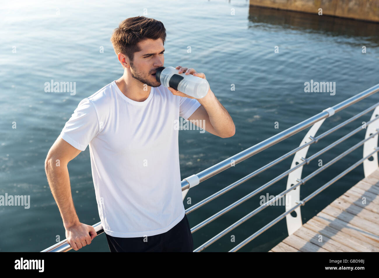 Attraktive junge Sportler stehen auf hölzernen Terrasse nahe dem Meer und Trinkwasser Stockfoto