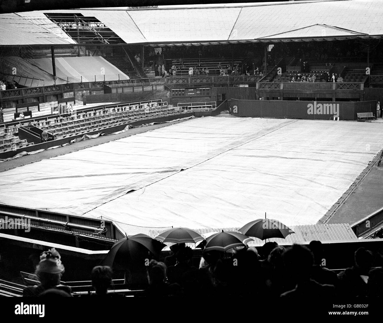 Tennis - Wimbledon Championships. Das Center Court ist bedeckt, wenn Regen auf den All England Club fällt (Bombenschäden aus dem Zweiten Weltkrieg sind in der linken oberen Ecke noch gut sichtbar) Stockfoto