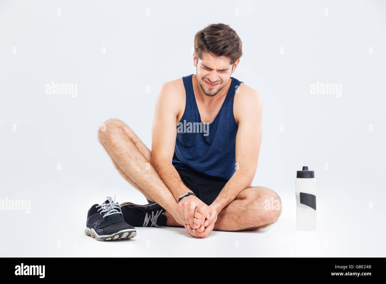 Fitness Mann sitzen und Leiden mit Fußschmerzen auf weißem Hintergrund Stockfoto