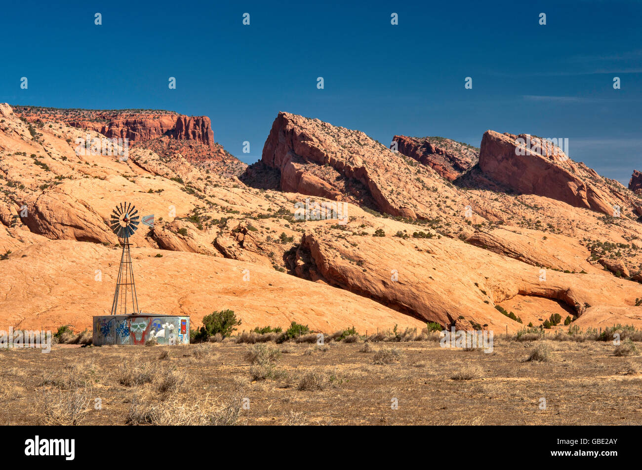 Alte Aermotor Windmühle und Wassertank, Skeleton Mesa Sandstein Slickrock dahinter, Navajo Indianerreservat, in der Nähe von Kayenta, Arizona, USA Stockfoto