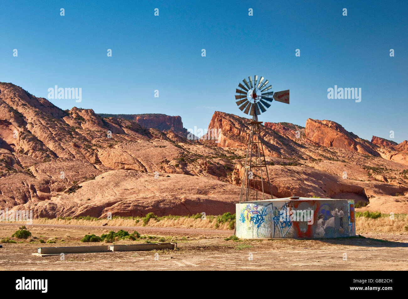 Alte Aermotor Windmühle und Wassertank, Skeleton Mesa dahinter, Navajo Indianerreservat, in der Nähe von Kayenta, Arizona, USA Stockfoto