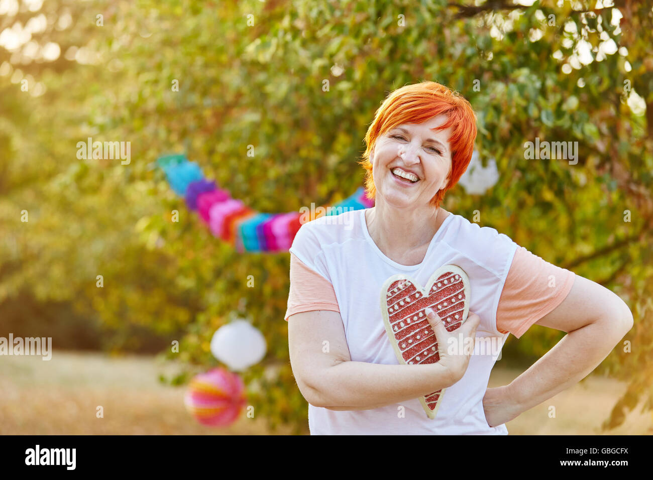 Glückliche ältere Frau mit einem Herz auf ihrer Hand im Sommer in einem park Stockfoto