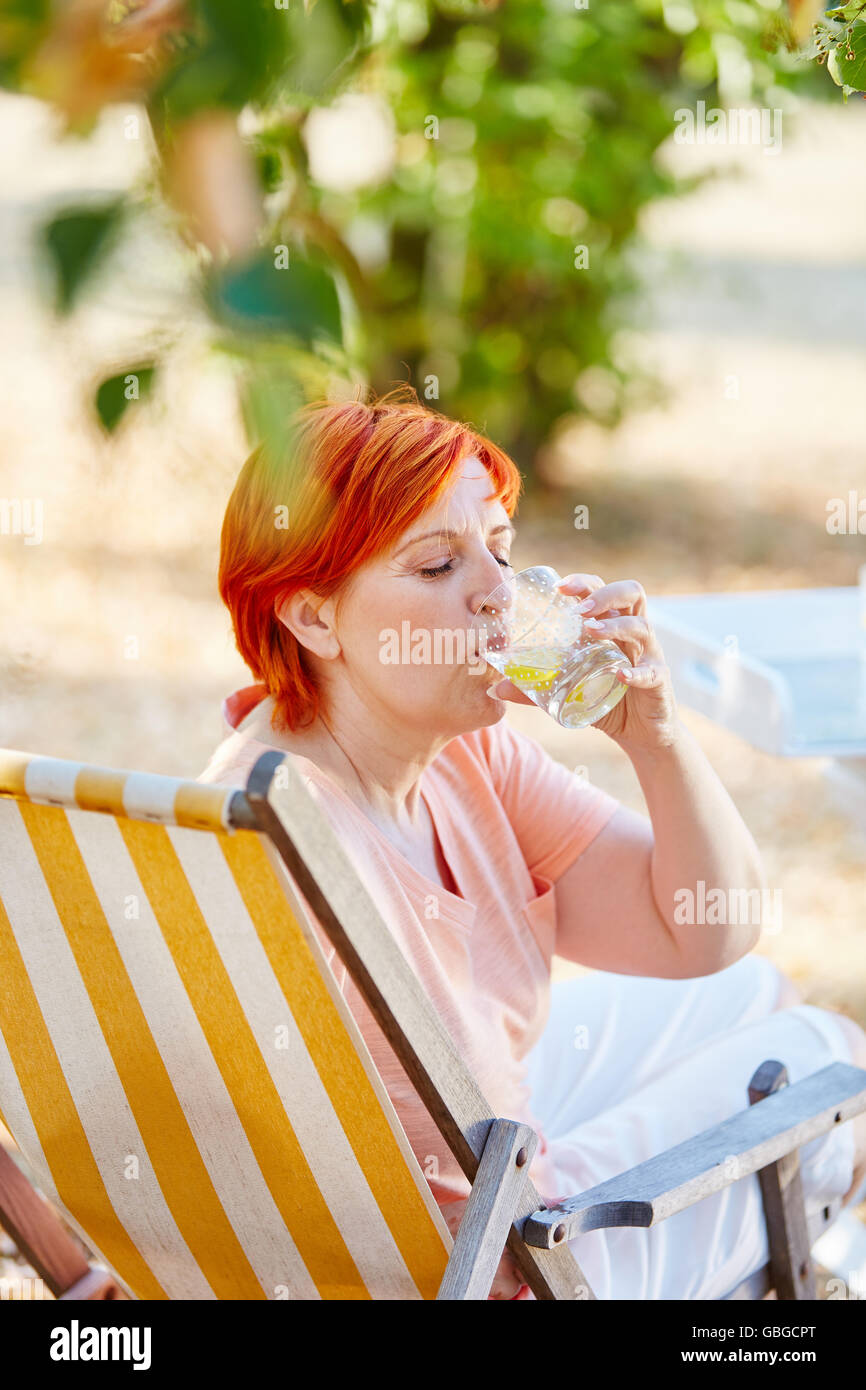 Ältere Frau trinkt ein Glas Wasser auf einem Liegestuhl im Sommer Stockfoto