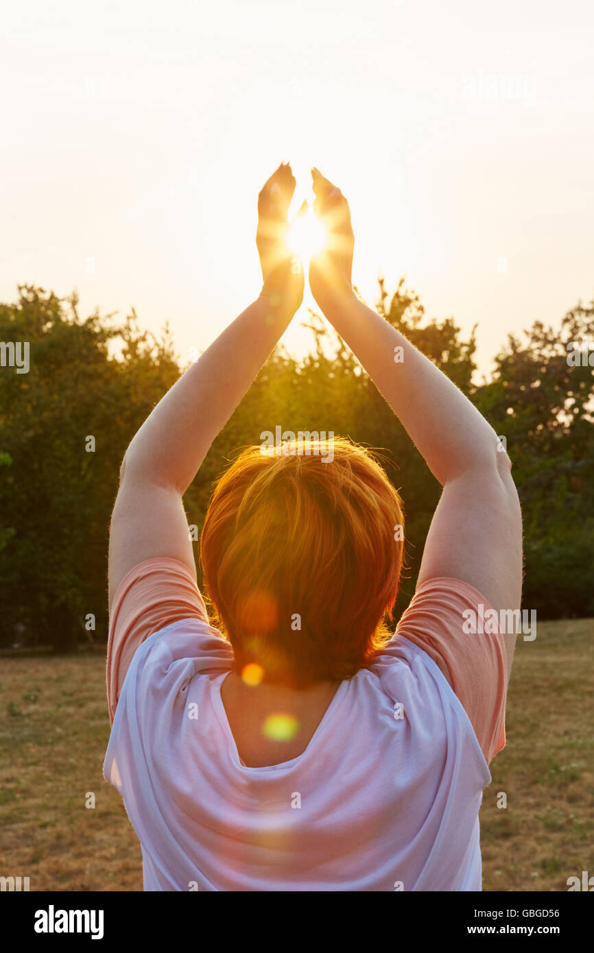 Ältere Frau macht eine Yoga-Meditation mit der Sonne in der Mitte ihrer Hände trainieren Stockfoto