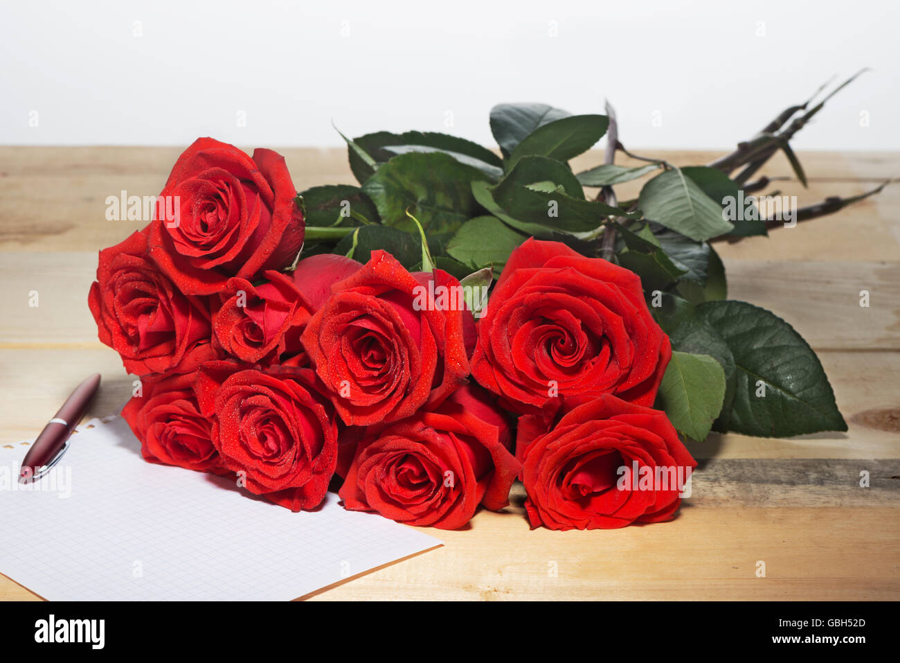 Bouquet von scarlet Rosen auf einer Fläche von Holzbrettern und das Blatt Papier schreiben des Textes Stockfoto