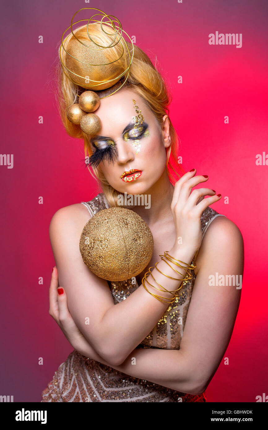Blonde Avantgarde kreative Make-up, gold Kugeln, Glitter Paillettenkleid, roten Hintergrund, Blattgold, architektonische Haar, Kopfbedeckung Stockfoto