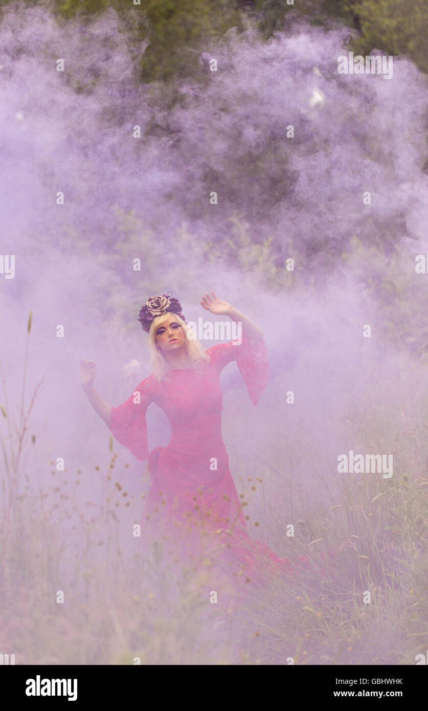 Blonde romantische Fee Elfe Modell in Wiese mit mit gold lila rose Krone Kopfschmuck, kontemplativen, lila Rauch Stockfoto