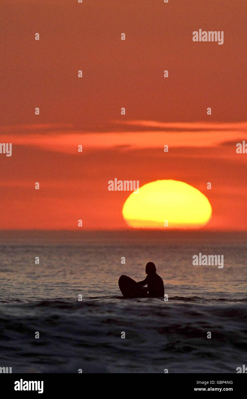 Ein einfarbiger Surfer wartet auf die letzten Wellen des Tages, wenn die Sonne in Woolacombe, North Devon, untergeht, während das warme Wetter in Großbritannien anhält. Stockfoto