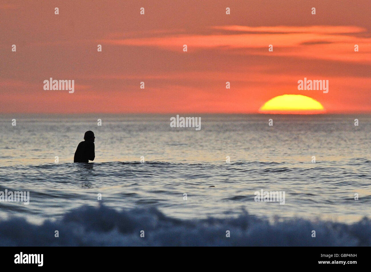 Ein einfarbiger Surfer wartet auf die letzten Wellen des Tages, wenn die Sonne in Woolacombe, North Devon, untergeht, während das warme Wetter in Großbritannien anhält. Stockfoto