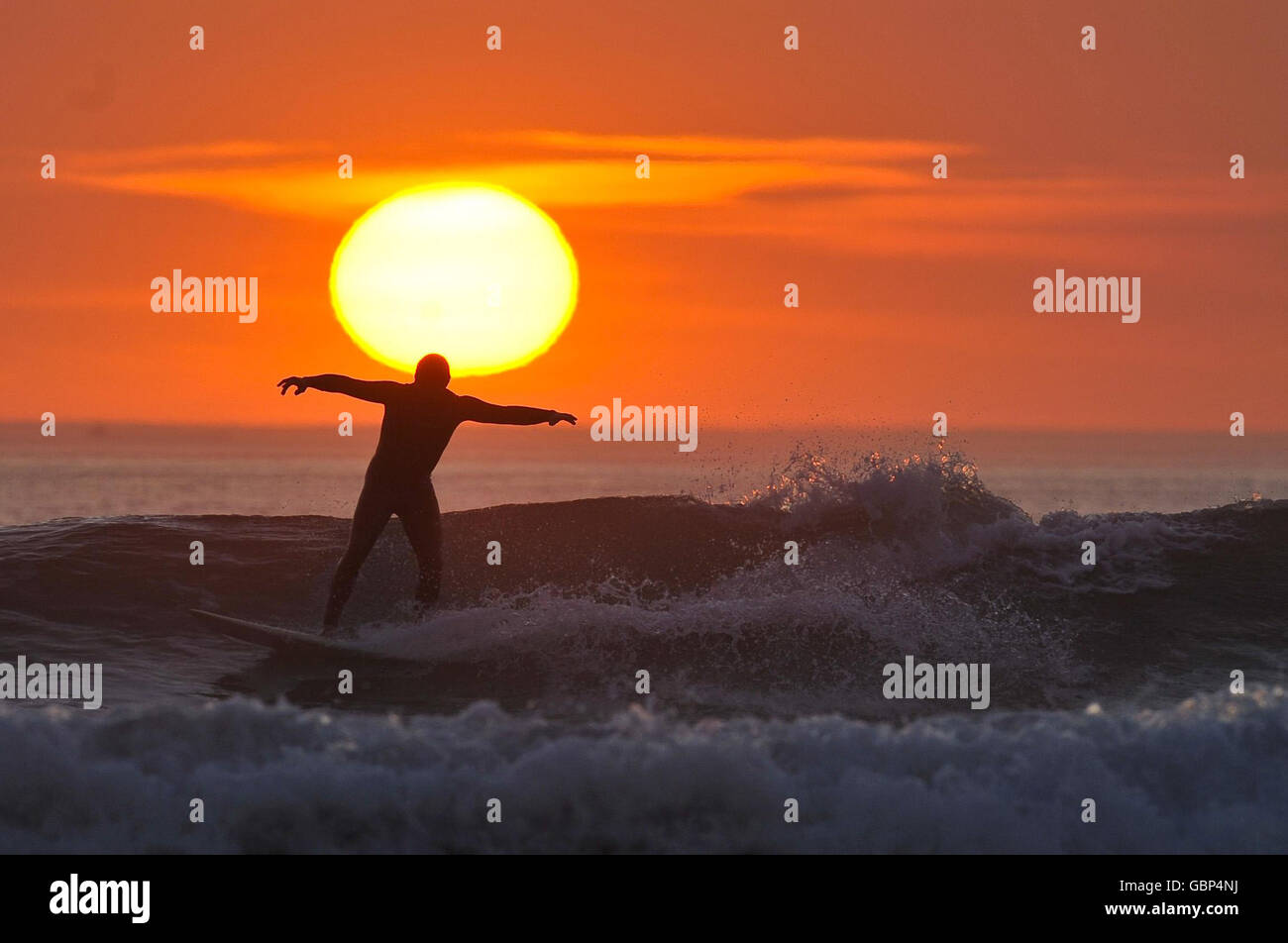 Ein einfarbiger Surfer genießt die letzten Wellen des Tages, wenn die Sonne in Woolacombe, North Devon, untergeht, während das warme Wetter in Großbritannien anhält. Stockfoto