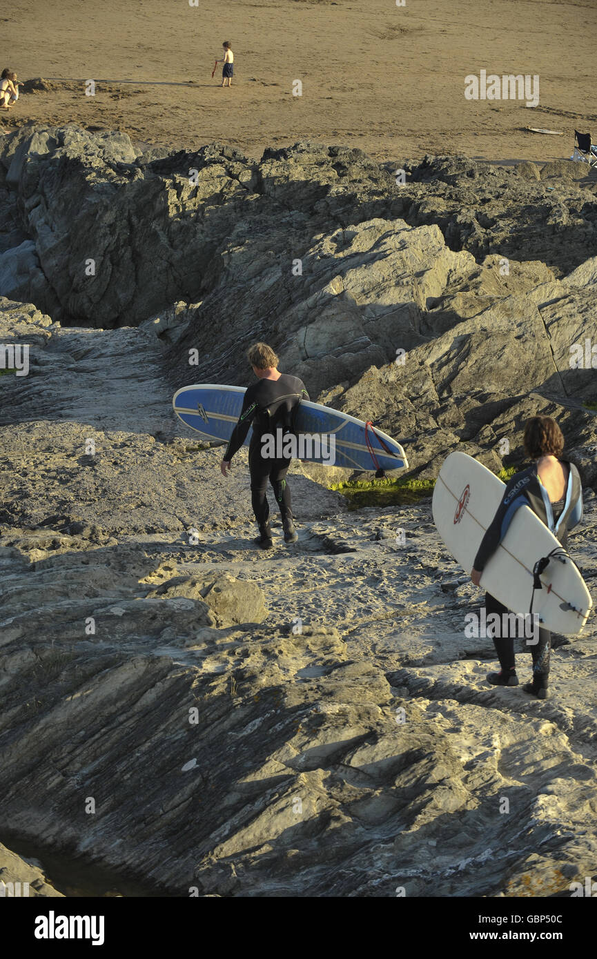 Zwei Surfer gehen einige Felsen in ihren Neoprenanzügen hinunter und bereiten sich vor Zum Surfen gehen Stockfoto