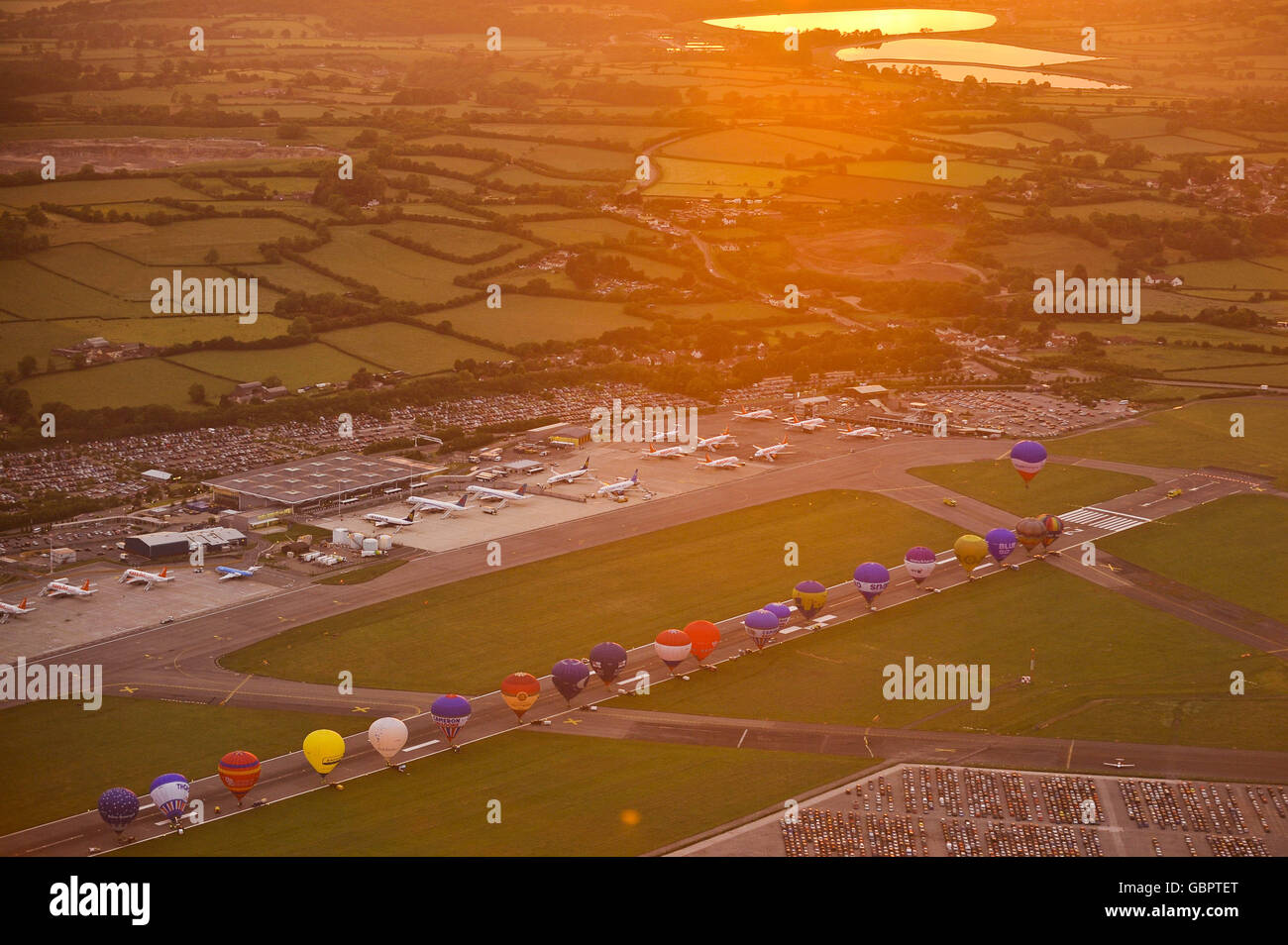 Heißluftballons stehen bei Sonnenaufgang auf der Hauptpiste des Bristol International Airport an, während sie sich zum ersten Mal auf den Flug vom Flughafen vorbereiten. Stockfoto