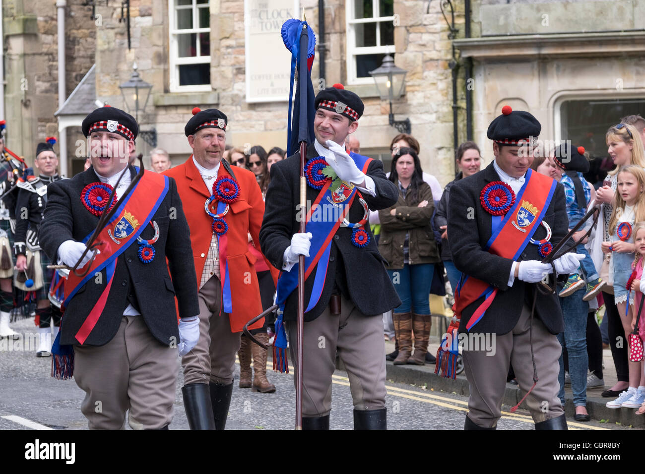 Jedburgh, UK. 8. Juli 2016.    Das Jethart Callant Festival, und gemeinsame Reiten, am 8. Juli 2016 in Jedburgh, Schottland. Callant Gary Hogg zusammen mit rechten Mann Grant Raeburn und Lefthand Mann Jack Fraser, beobachtet von Herold Brian Marshall (in Jagd rot) zum Abschluss der Morgen-Zeremonien, Prost und Wellen für die Massen. Fast 270 angebrachten Anhänger nahmen an der Fahrt Teil.  Bildnachweis: Rob Gray/Alamy Live-Nachrichten Stockfoto