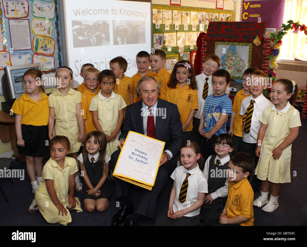 Sir Jackie Stewart erhält eine Geburtstagskarte von Schülern der Knoxland Primary School während einer Zeremonie, bei der er während einer offiziellen Zeremonie zum Freeman of West Dunbartonshire gemacht wurde. Knoxland Primary School. Stockfoto