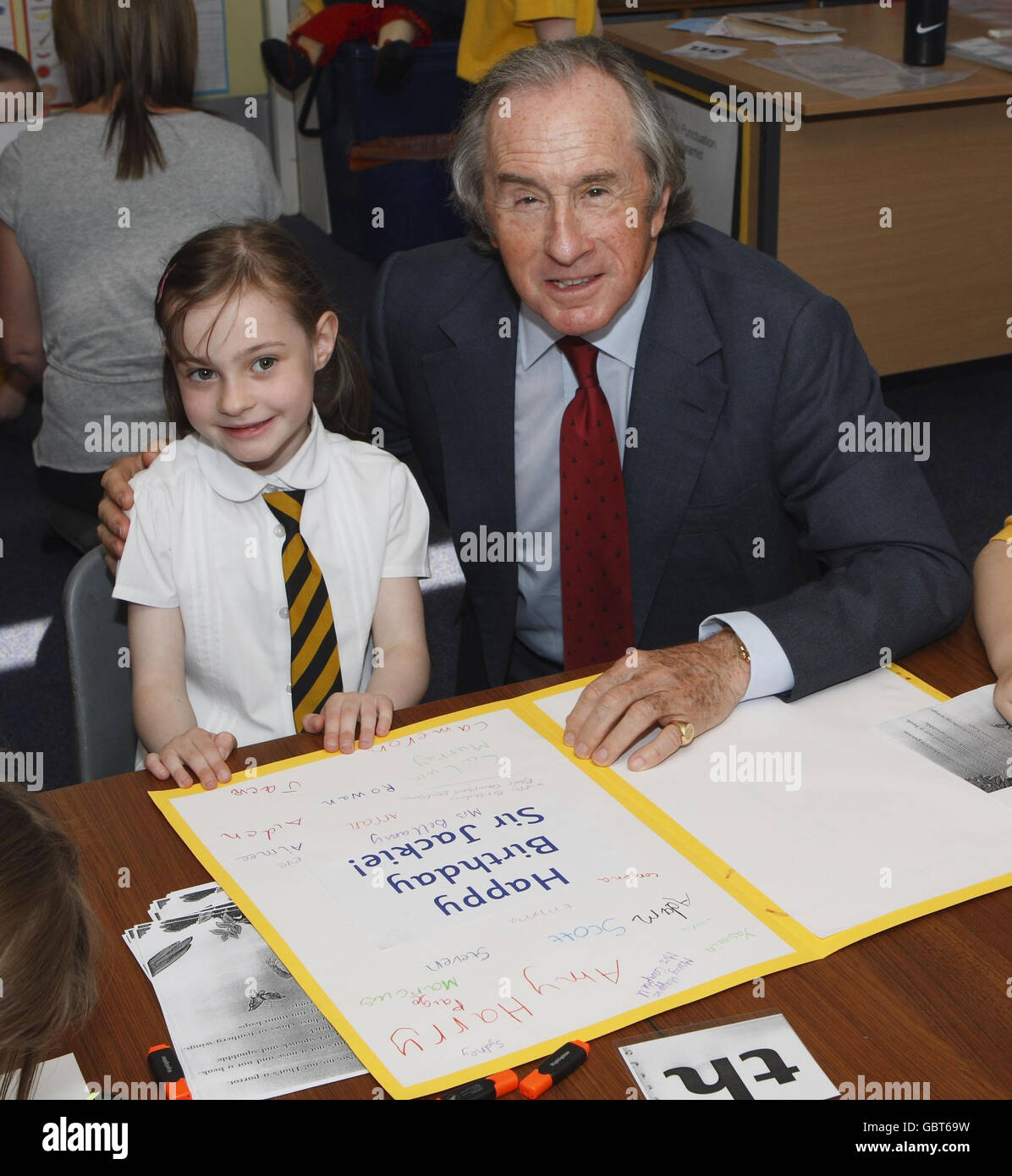 Sir Jackie Stewart erhält eine Geburtstagskarte von der Schülerin Eve Allen von der Knoxland Primary School, während einer Zeremonie, bei der er während einer offiziellen Zeremonie zum Freeman of West Dunbartonshire gemacht wurde. Knoxland Primary School. Stockfoto