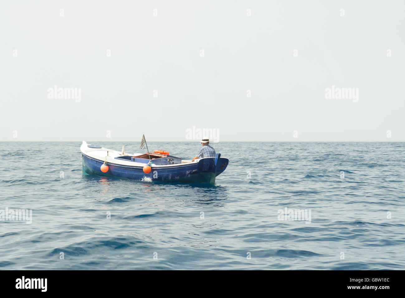 Mann in Panama Strohhut in blauen Holzboot auf dem Meer in Griechenland Stockfoto