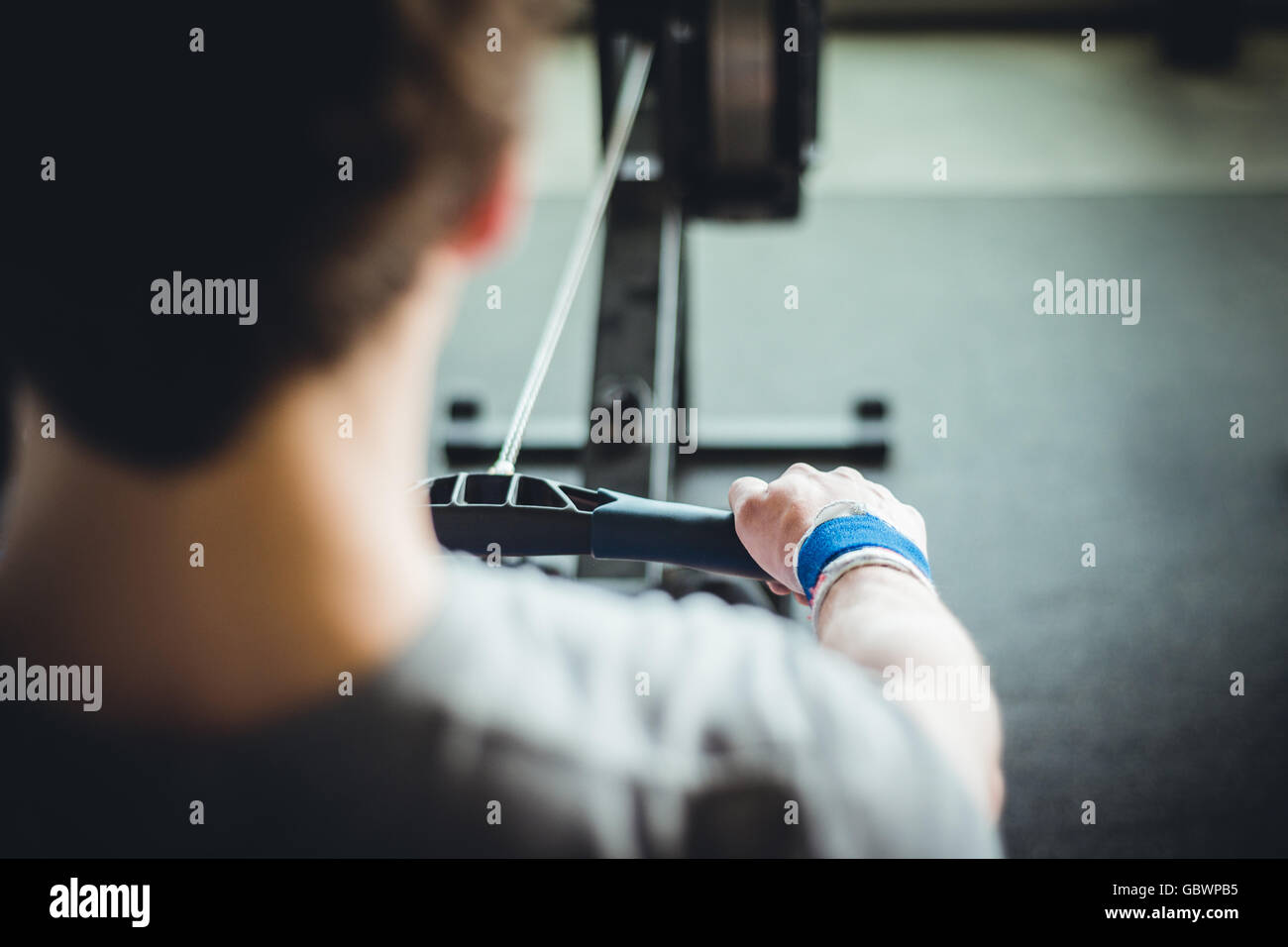 DER JUNGE Mann in den Zwanzigern, der sich auf der Rudermaschine aufwärmte. Stockfoto