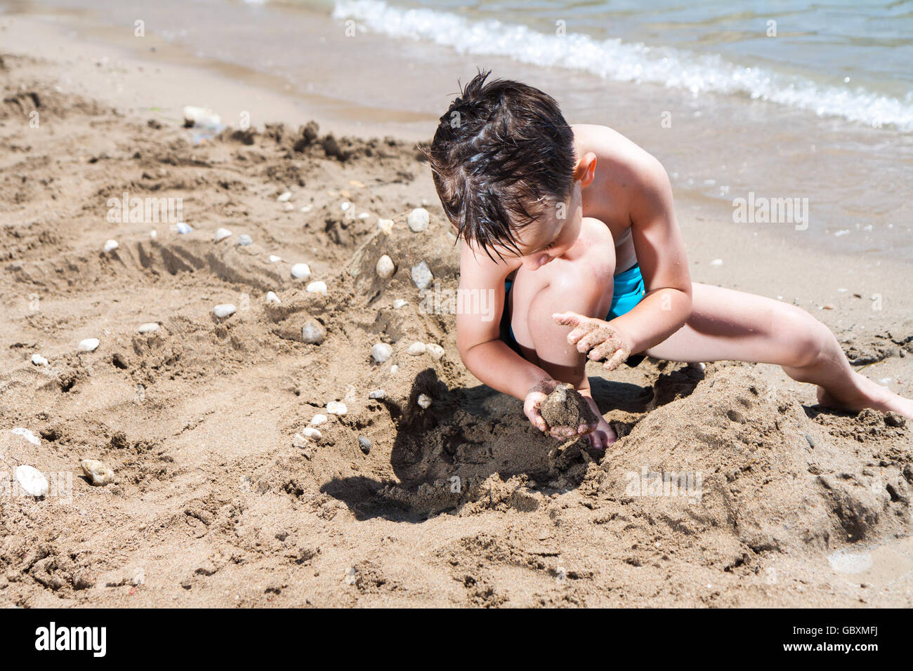 kleiner Junge im blauen Meer mit Sandkuchen und Sand spielen Stockfoto