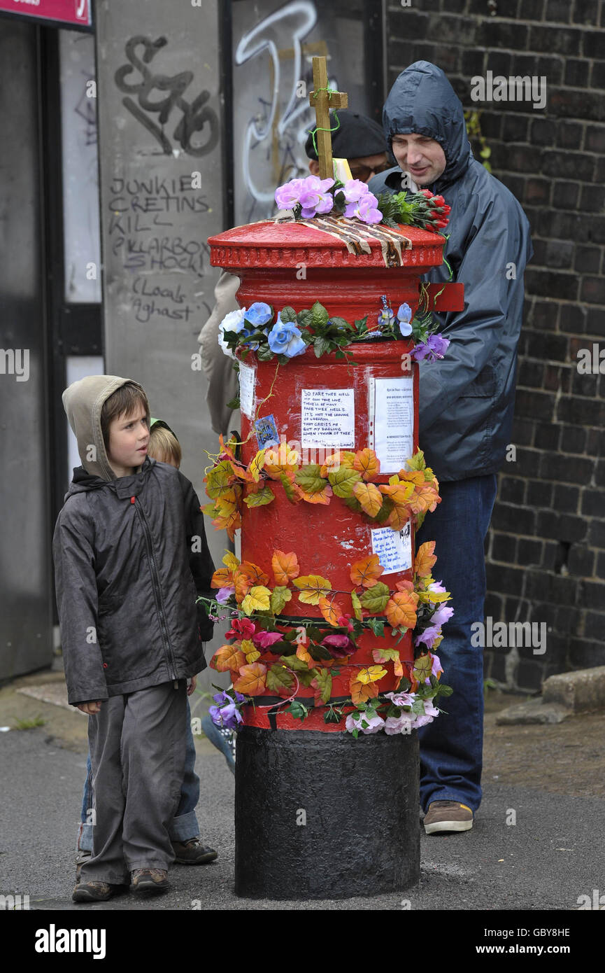 Die Leute schauen sich die Nachrichten auf einem Briefkasten in Bedminster, Bristol, an, der der öffentlichen Nutzung entzogen wurde. Der Briefkasten wurde nach der Schließung durch die Royal Mail zu einem Kunstwerk, geschmückt mit Poesie, Blumen und religiösen Insignien, gemacht. Stockfoto