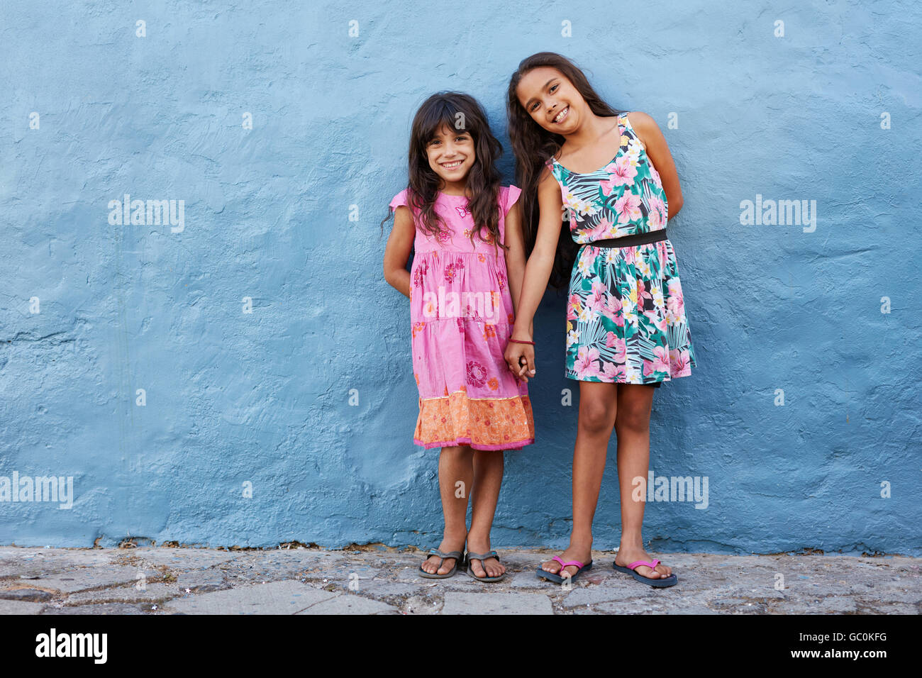 In voller Länge Portrait von beiden schönen Mädchen zusammenstehen gegen blaue Wand. Niedliche kleine Mädchen posieren zusammen mit s Stockfoto