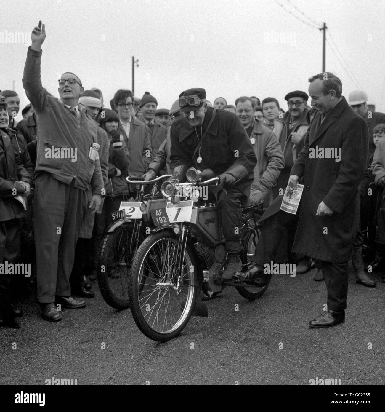 John Surtees (stehend, rechts), der Weltmeister auf zwei Rädern war und der aktuelle Weltmeister auf vier Rädern ist, freut sich über ein paar leichtherzige Kommentare mit Rider V.F. Smith (Vorname unbekannt) von Barnes Common, bevor er beim 29. Pioneer Run von Tattenham Corner, Epsom, Surrey, nach Brighton aufbricht. Smith fuhr auf einem 1904 396 ccm großen Solo-Quadranten. Stockfoto