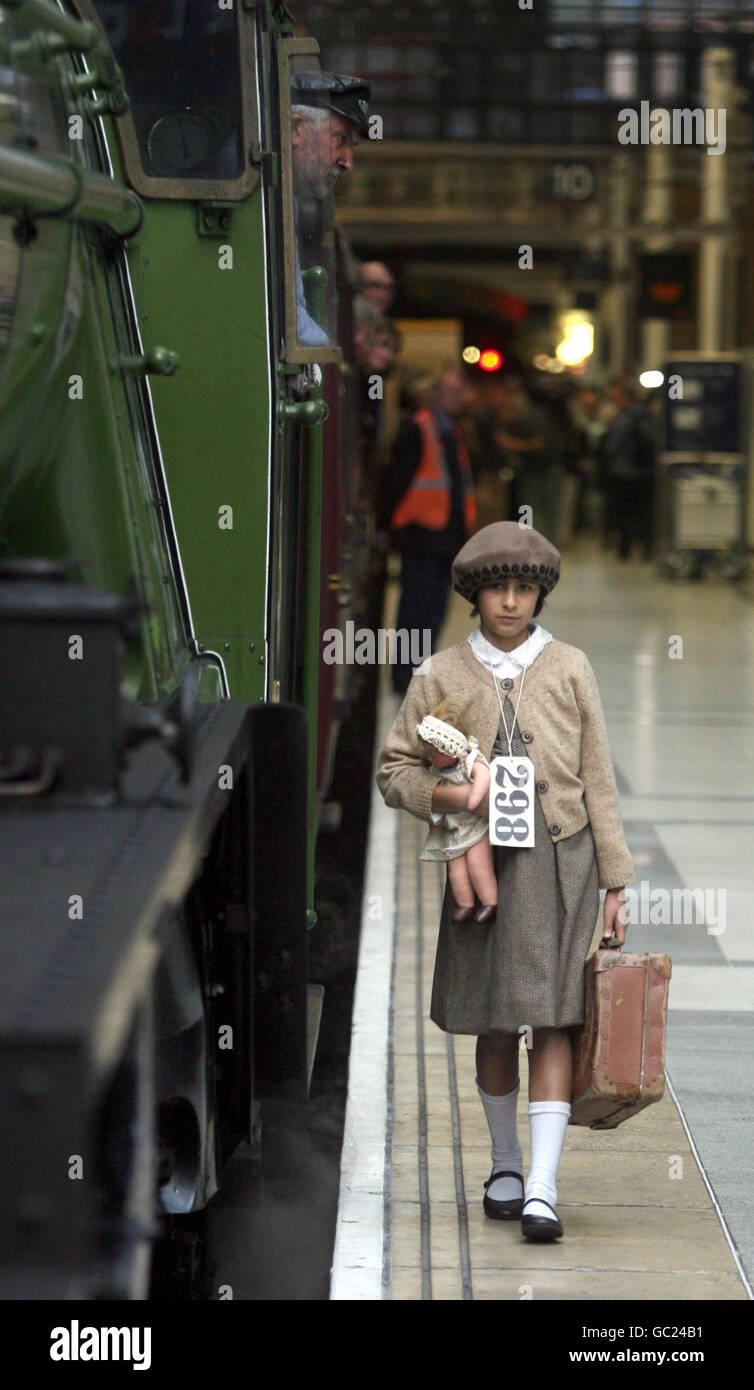 Ein junges Mädchen, das als Flüchtling aus dem Zweiten Weltkrieg gekleidet ist, geht am Winton Train an der Liverpool Street Station in London vorbei. Stockfoto