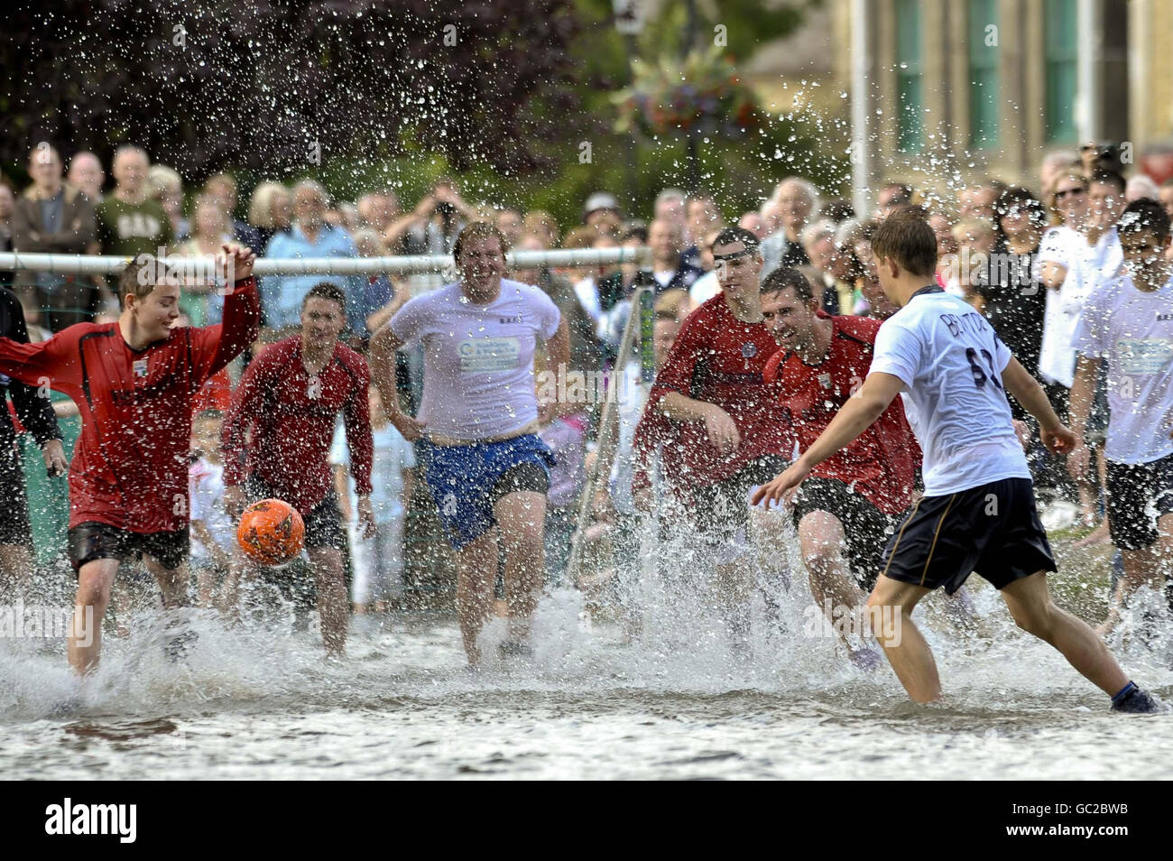 Die Spieler von Bourton Rovers kämpfen beim jährlichen Fußballspiel im River Windrush im Zentrum des Dorfes Gloucestershire als erstes Team gegeneinander. Stockfoto