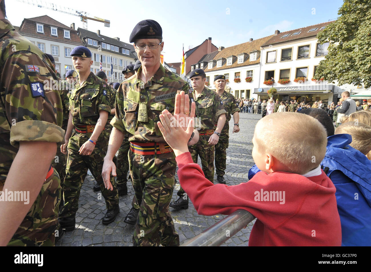 Ein kleines Kind gibt einem Soldaten eine "hohe fünf", nachdem er von der Parade "ausgefallen" ist und Soldaten gehen zu einem Gottesdienst, da über 500 Soldaten der 20. Panzerbrigade - der Eisernen Faust - ihre Rückkehr von Operationen im Irak markieren, Afghanistan und Kosovo bei einer Parade durch die Garnisonsstadt Paderborn vor hunderten Zuschauern aus der deutschen Gemeinde und den Familien und Freunden der Soldaten. Stockfoto