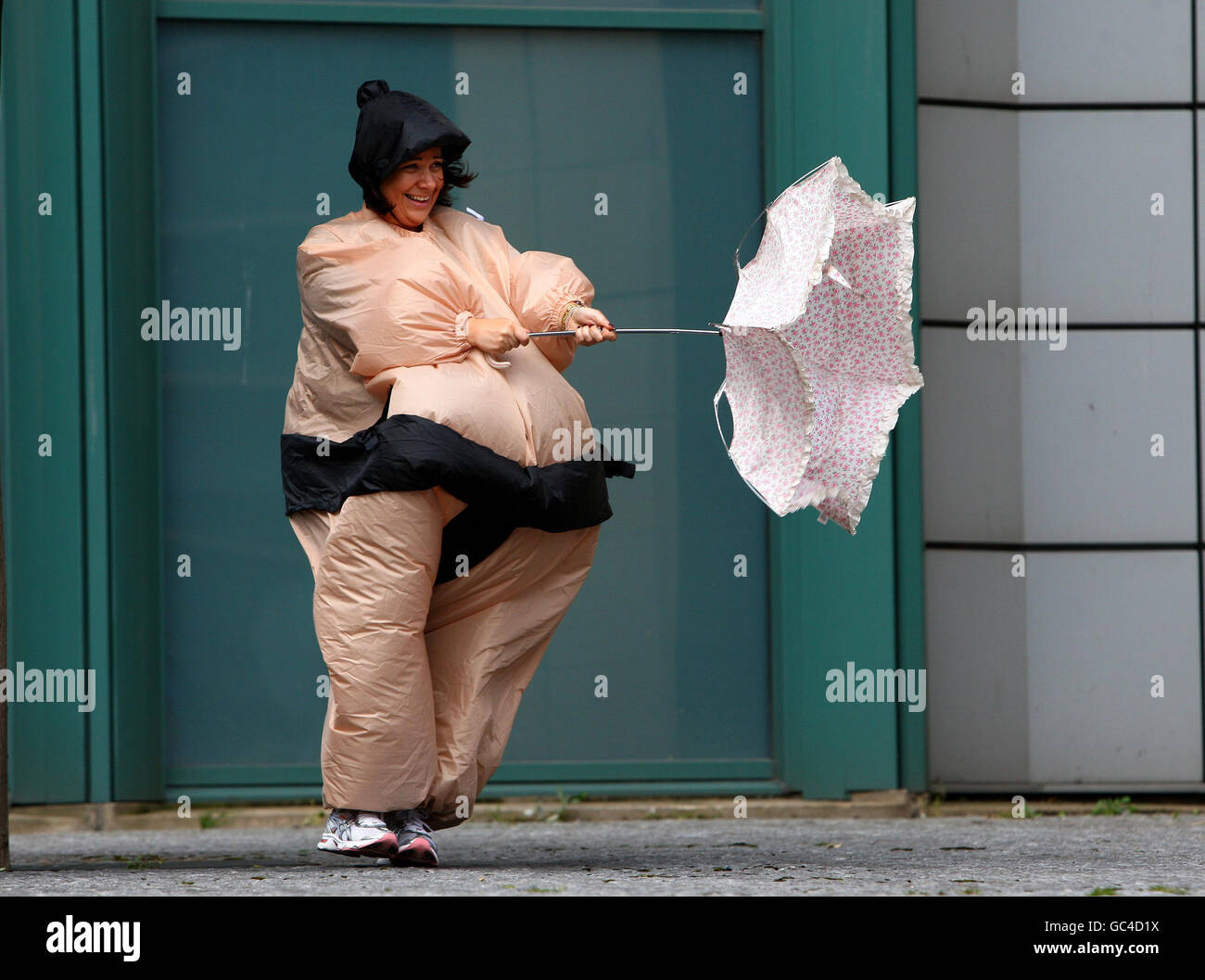 Alex Mickelson in einem Sumo-Ringer-Anzug kämpft mit einem Regenschirm im Wind auf dem Edinburgh Festival Square und hilft, Geld zu sammeln, indem er eine Meile läuft, was bis zu 500 Meilen für das Miles for Smiles-Event summieren wird. Stockfoto