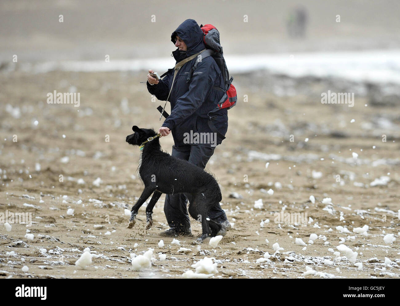 Ein Mann und sein Hund trotzen den Elementen in Putsborough, North Devon, wo starke Winde große schäumende Wellen im Meer verursacht haben. Stockfoto