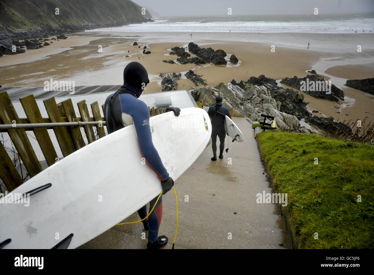Surfer gehen in Neoprenanzügen, Stiefeln, Handschuhen und Mützen in Putsborough, North Devon, ins Meer, wo starke Winde große Wellen verursacht haben. Stockfoto