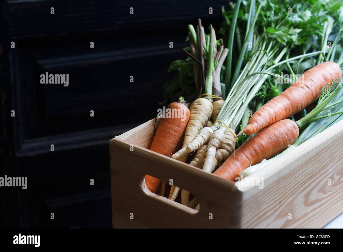 große hölzerne Kiste voller roh, frisch geerntet, Gemüse auf dunklem Hintergrund Stockfoto