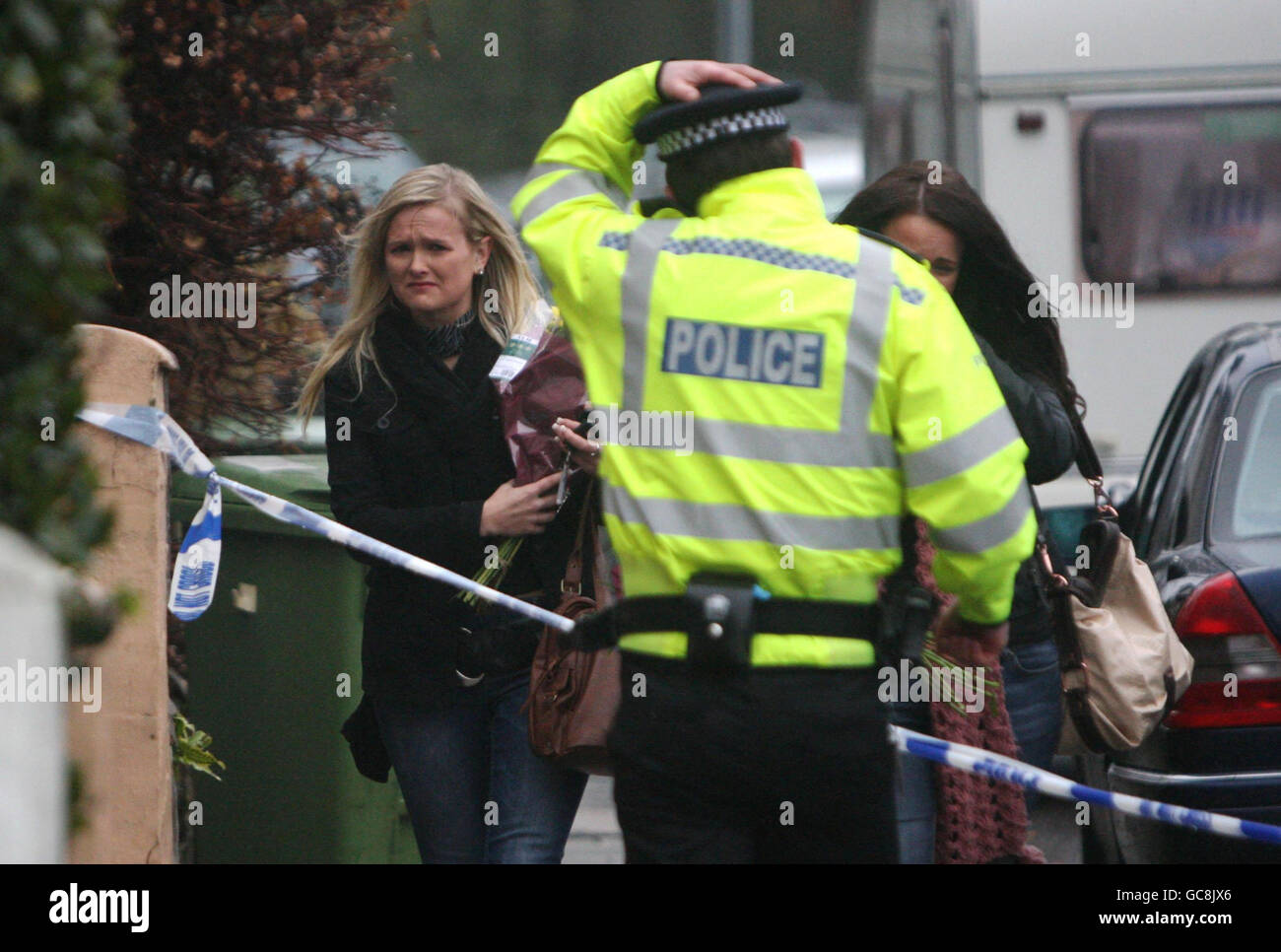 Trauernde sprechen mit der Polizei, während sie Blumen an den Ort bringen, an dem ein vierjähriges Mädchen und ihr Vater gestern tot in einem Haus in Aldershot, Hampshire, gefunden wurden. Stockfoto