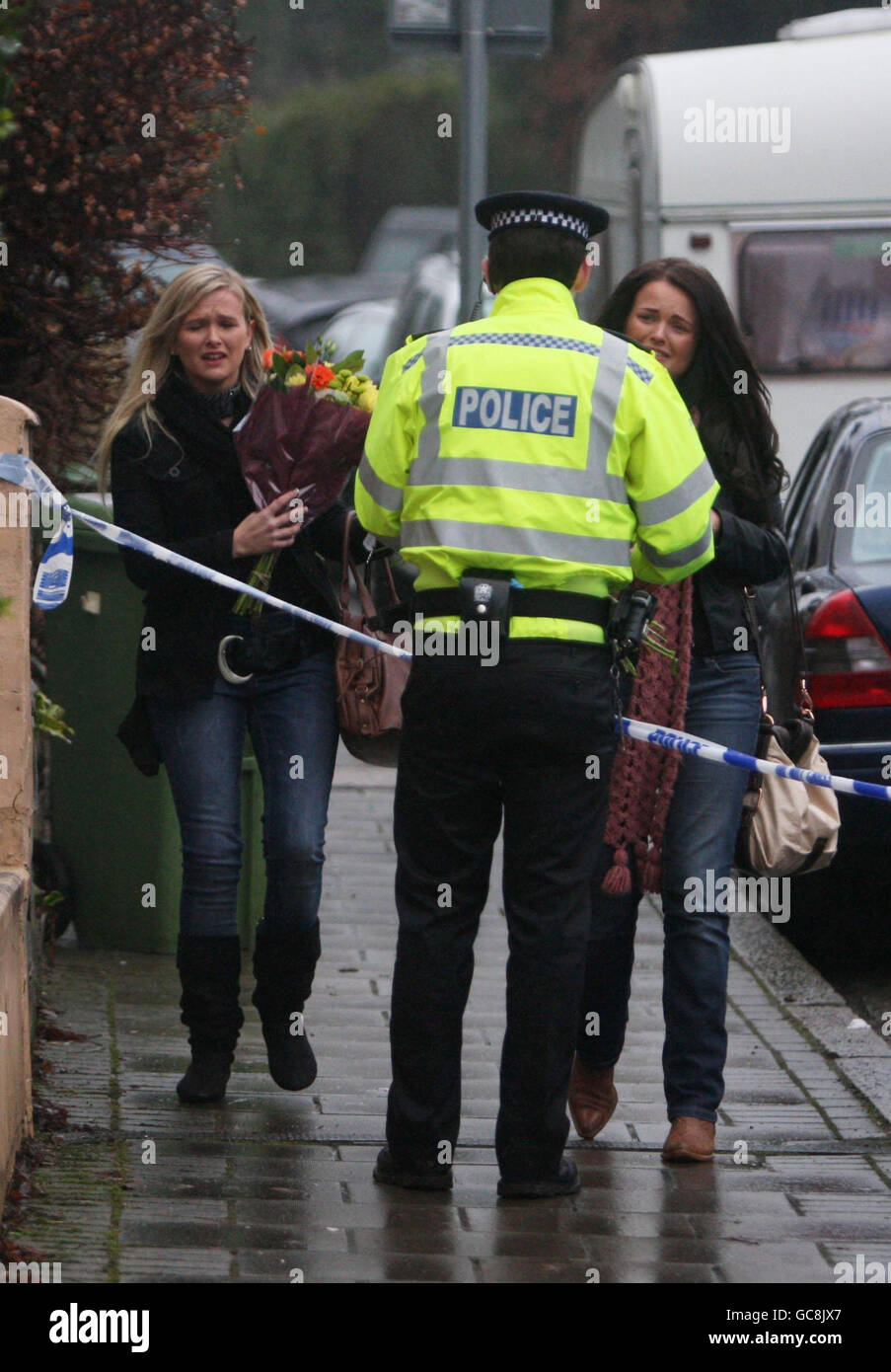 Trauernde sprechen mit der Polizei, während sie Blumen an den Ort bringen, an dem ein vierjähriges Mädchen und ihr Vater gestern tot in einem Haus in Aldershot, Hampshire, gefunden wurden. Stockfoto