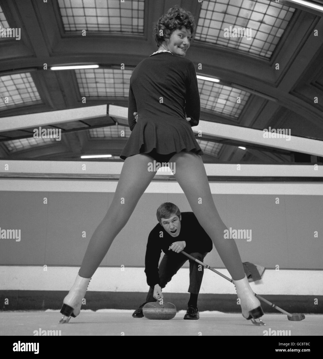 Umrahmt von den Beinen eines Eisläufern bereitet sich Billy Walker darauf vor, einen Stein auf den Weg zur Richmond Ice Rink zu schicken. Der Schwergewichtboxer Billy Walker hat sich am 6. Dezember in der Royal Albert Hall, London, mit dem Curling als Entspannung vom Training für den Kampf mit Ray Patterson, Bruder von Floyd, beschäftigt. Stockfoto