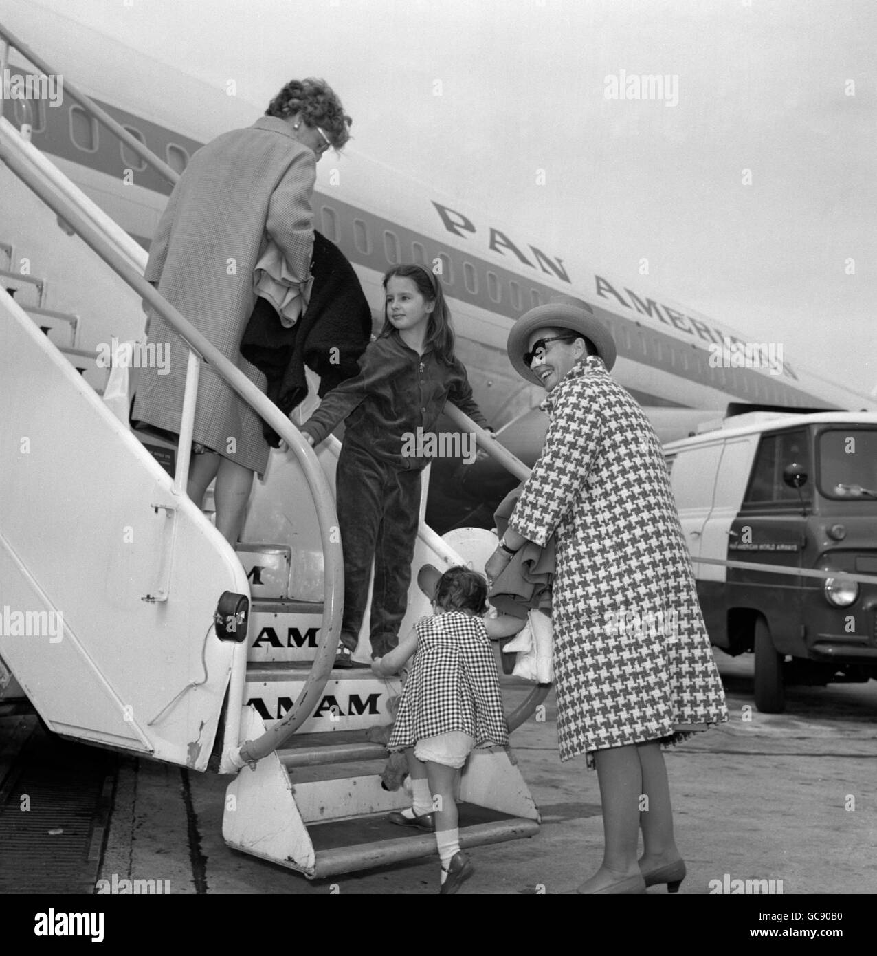 Die in Großbritannien geborene Schauspielerin Jean Simmons trägt einen Mantel aus fetten Karos und hilft ihrer zweijährigen Tochter Kate heute lächelnd an Bord eines Pan American Liners am Flughafen London, als sie mit ihren Kindern nach Kalifornien zurückkehrte. Stockfoto