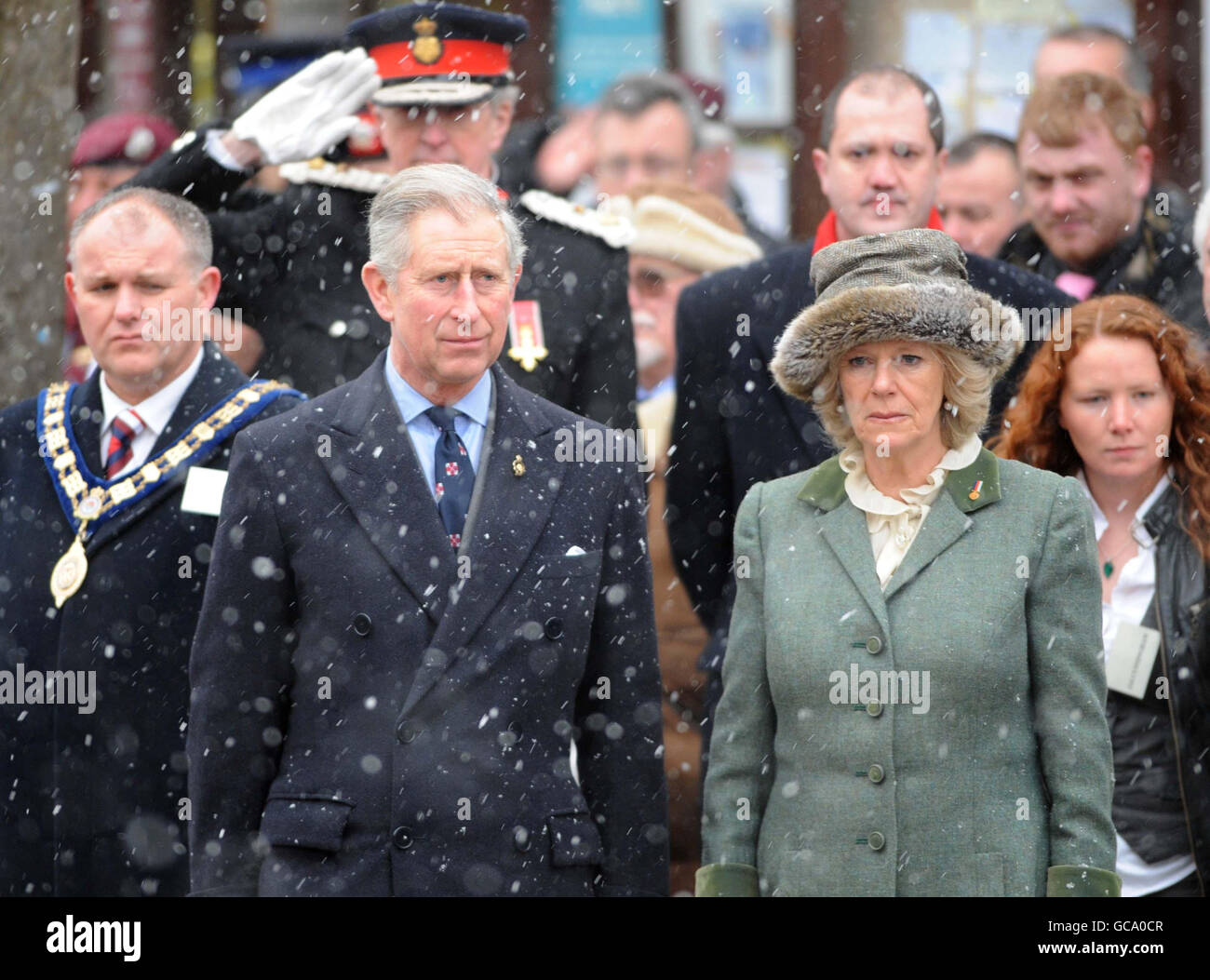 Der Prinz von Wales und die Herzogin von Cornwall stehen im Schnee während einer Kranzniederlegung in Wootton Bassett, Wiltshire, während eines Besuchs in der Stadt. Stockfoto