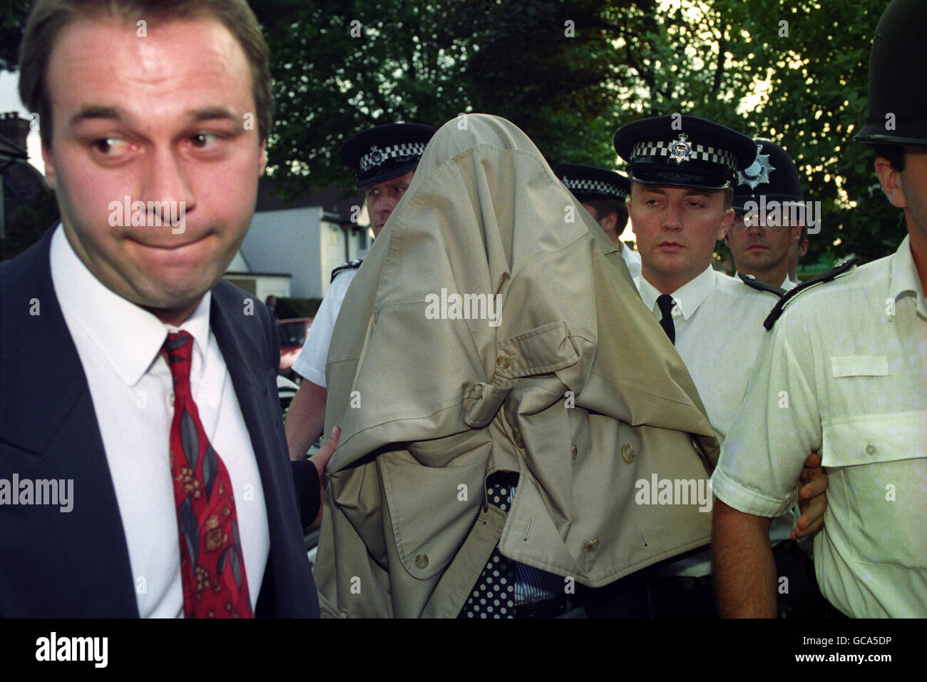 DER POLIZEIBUCHHALTER TONY WILLIAMS, DER VON EINEM MANTEL BEDECKT IST, VERLÄSST SEIN NEUES HAUS IN MALDEN, BEGLEITET VON POLIZISTEN. Stockfoto