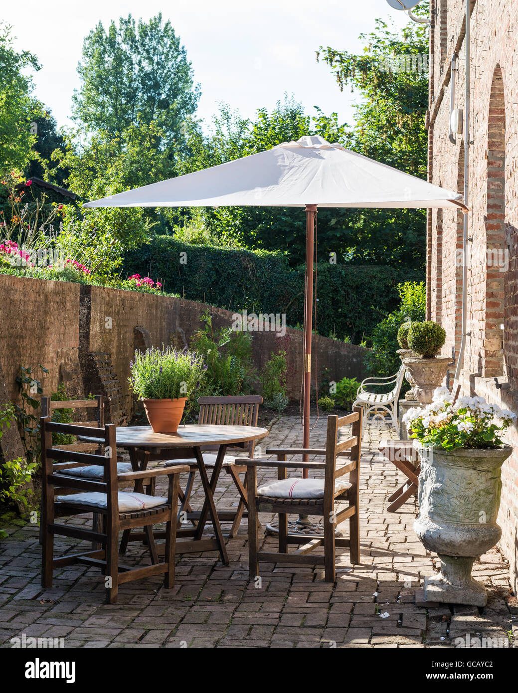 Teakholz-Gartenmöbel und Steinurnen auf gemauerten Sonnenterasse mit Sonnenschirm Stockfoto