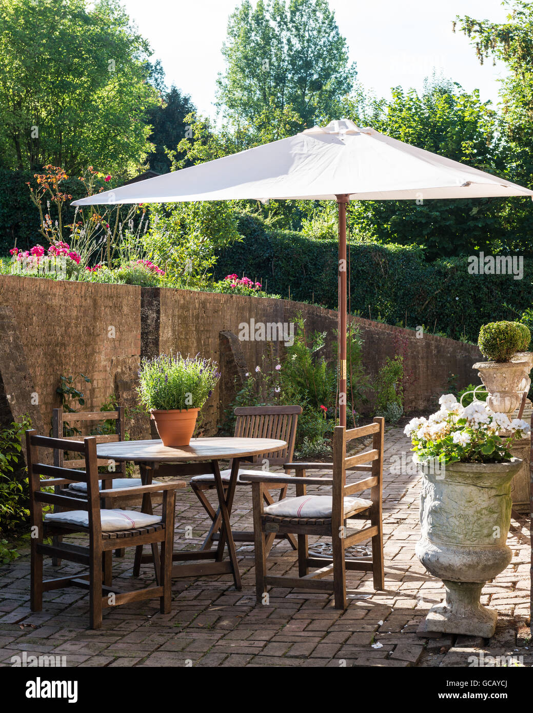 Teakholz-Gartenmöbel und Steinurnen auf gemauerten Sonnenterasse mit Sonnenschirm Stockfoto