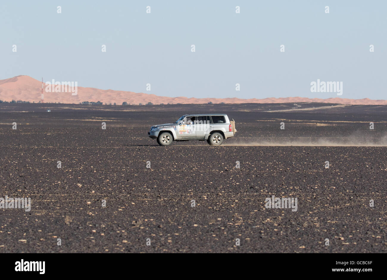 Range Rover Reisen in Marokko Steinwüste, von rechts nach links, Richtung Silber blauer Himmel und Berge im Hintergrund. Stockfoto